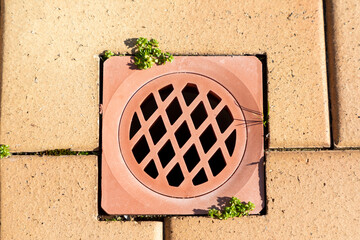 A stormwater drain cover inserted in brown paving stones