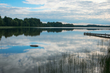 A quiet lake with a reflection of clouds and an old wooden footbridge