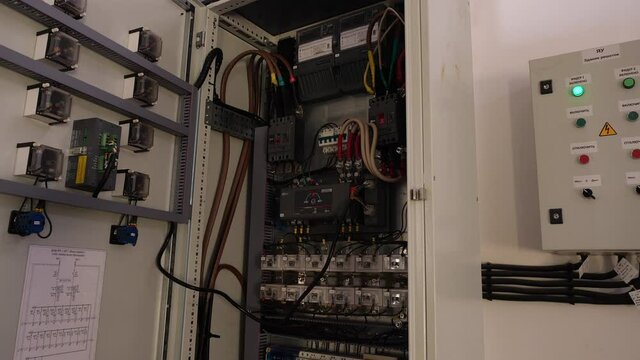 Switchboard with breakers cables and meters in control cabinet on light wall in spacious plant workshop close view