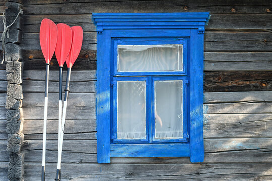 Red plastic paddles bent over old rustic wooden hut with blue painted window.