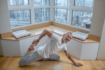 Gray-haired man in a white tshirt doing yoga and looking involved