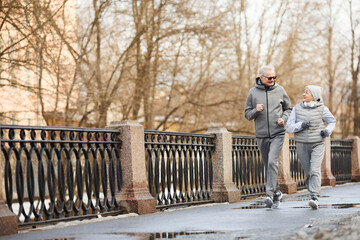 Full length wide angle view at active senior couple running outdoors in winter