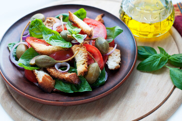 Italian Panzanella salad with bread, tomatoes, basil, capers and olive oil on brown plate on round wooden board