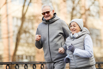 Waist up portrait of active senior couple running outdoors in winter and smiling happily, copy space