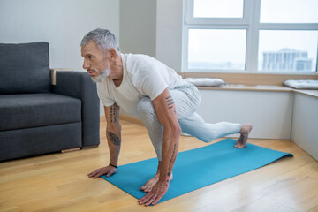 A mature man practising yoga at home and looking concentrated