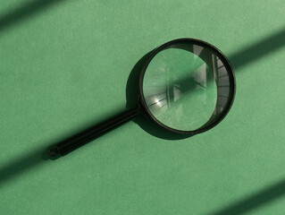 Magnifying lens over green background with sunlight and shadow stripes. Magnifier concept.