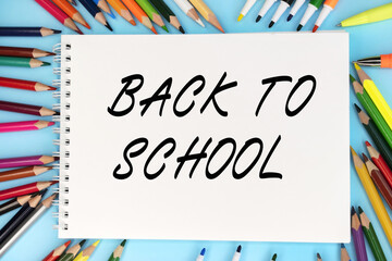 Back to school is written on a notebook that lies on a blue background among colored pencils and markers. Educational concept