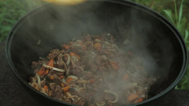 meat stewed with onions and carrots. zucchini is added to the dish and mixed with a wooden spoon