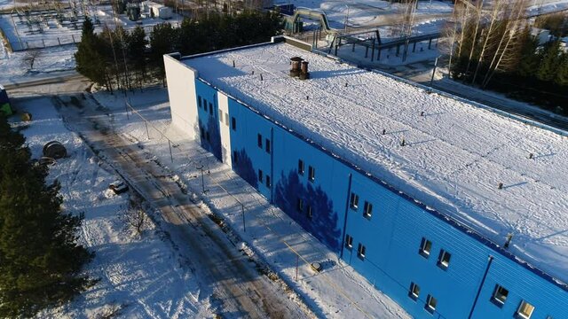 Blue workshop building with snow on flat roof at wastewater treatment plant at sunset in winter evening aerial view