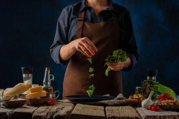 Caesar salad. Cooking process. The chef adds chunks of lettuce to the dish. The products on the table are used in the classic Caesar salad recipe.