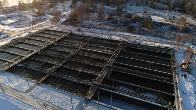 Group of pools with aerated water and bridges at treatment plant on snowy hill at sunset in winter bird eye view