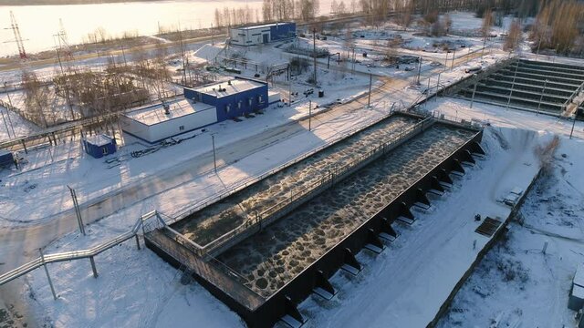 Large tanks with aerated water and empty bridge at modern purification station at sunset in winter aerial view