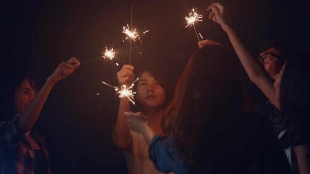 Group of Asia best friends teenagers play firecracker dancing have fun enjoy party with happy moments together in national park campsite at night. Beautiful bonfire camping traveller concept.