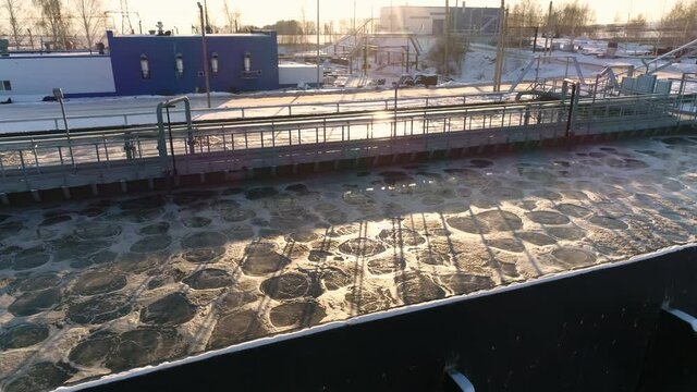 Basin with swirling water at aeration and empty bridge near workshop at filtration station at sunset in winter aerial view