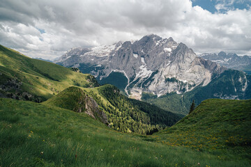 Fototapeta premium Summer view of Marmolada (Punta Penia), the highest peak in Dolomites, Italy. Alpine landscape of Dolomiti with a view of a glacier on Marmolada and beautiful green meadow with yellow flowers.