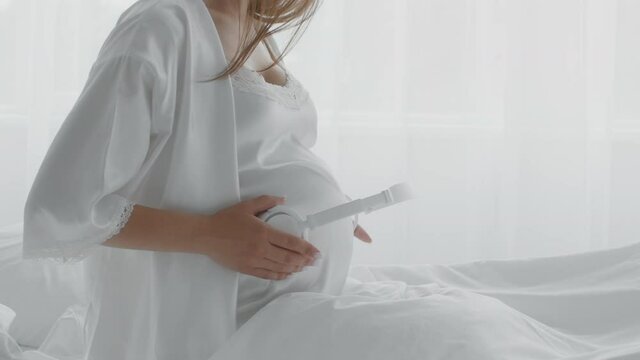 Pregnant Woman Holding Headphones Near Belly, Playing Music To Baby In Womb