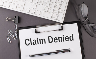 Office paper sheet with text CLAIM DENIED with office tols and keyboard. Business