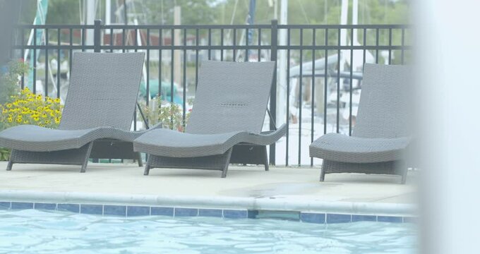 A trio of empty chaise lounge chairs outside on the deck next to the empty swimming pool free of people practicing social distancing during the pandemic 
