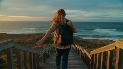 Cinematic inspiring shot of young woman run down epic boardwalk down to rocky ocean coastline. Female adventurer explore sunset coast. Scenic vacation travel destination. Wanderlust lifestyle - Powered by Adobe
