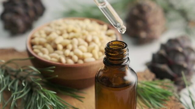 Pine essential oil with pine cones and nuts dripping from pipette to the bottle.