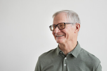 Minimal portrait of smiling senior man looking away while standing against white background, copy...