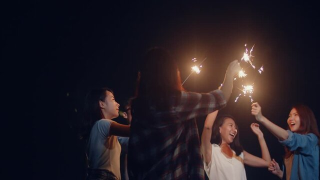 Group of Asia best friends teenagers play firecracker dancing have fun enjoy party with happy moments together in national park campsite at night. Beautiful bonfire camping traveller concept.