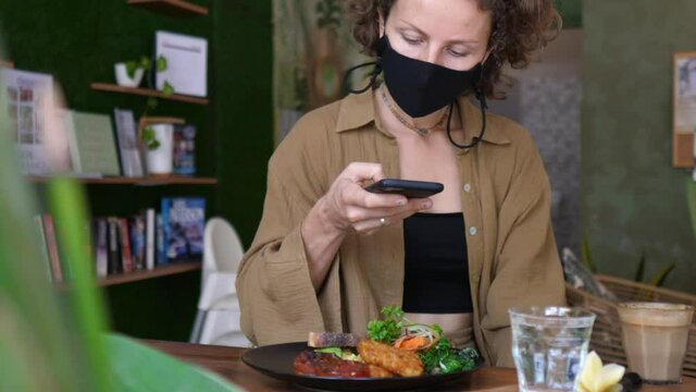Caucasian female food blogger in a face mask taking pictures of her plant based lunch 