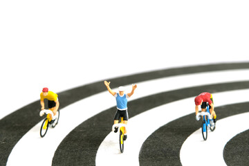 Miniature people toy figure photography. Bike cycling track. A biker cycling above dartboard,...