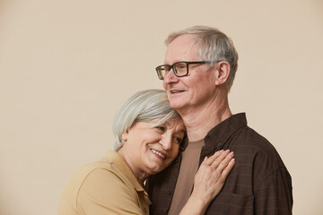 Minimal portrait of loving senior couple embracing against beige background, copy space