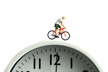 Miniature people toy figure photography. Cycling schedule concept. A biker cycling above clock, isolated on white background.