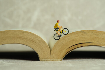Miniature people toy figure photography. Creative concept. A biker cycling above book opened