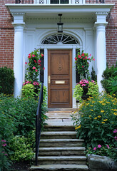 Portico entrance with elegant wood grain front door surrounded by colorful summer flowers