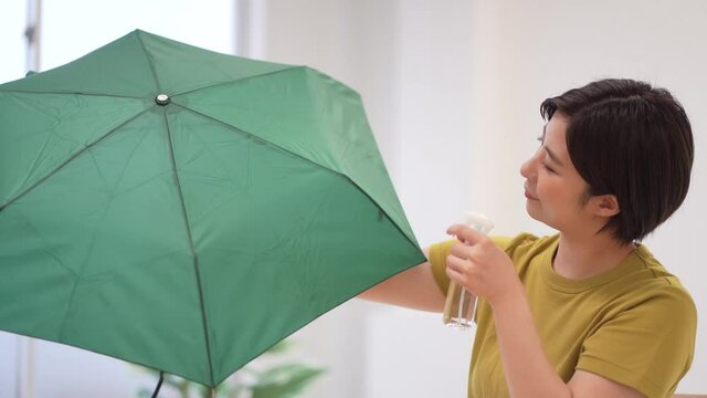 折り畳み傘に撥水スプレーを吹きかける女性