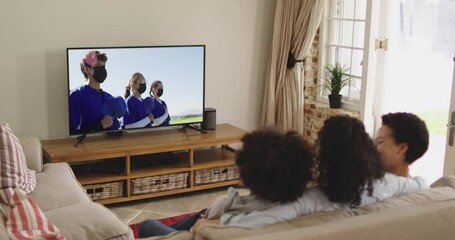 Composite of happy family sitting at home together watching baseball game during covid 19 on tv - Powered by Adobe