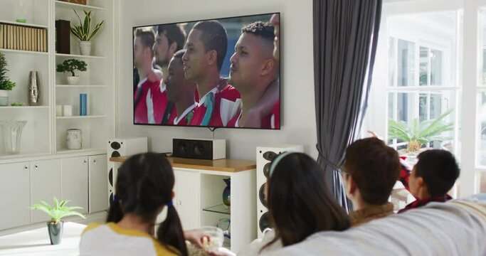 Composite of happy family sitting at home together watching sports event on tv