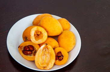 Ripe loquats in white dish on rustic wooden background with cut showing inside with seeds. (Eriobotrya japonica). loquat fruits