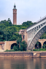 Bronx, NY - USA - July 17, 2021: Vertical view of the historic High Bridge spanning the Harlem River and Highbridge Water Tower is the distance. - obrazy, fototapety, plakaty
