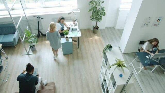High angle view of employees men and women working in office talking walking using computers. Creative workspace and businesspeople concept.
