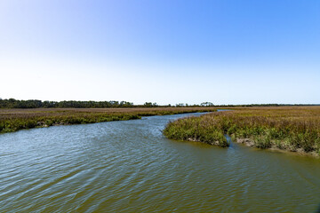 Salt marsh waterway with blue sky reflected in moving tidal water, horizontal aspect