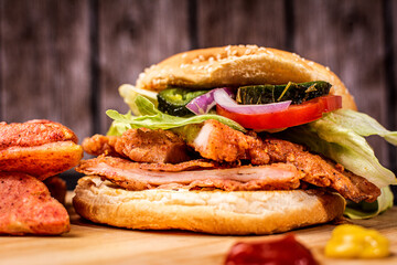 BREADED CHICKEN TORTA WITH LETTUCE, TOMATO AND CHILI, SERVED ON A WOODEN BASE, ACCOMPANIED BY FRENCH FRIES, KETCHUP AND MUSTARD.