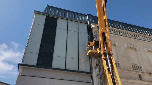 A Painter uses a Crane Lift To Paint the wall of a monument, France, Handheld shot