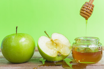 Jewish holiday, Apple Rosh Hashanah, the photo have honey in jar and drop honey on green apples on wooden with green background