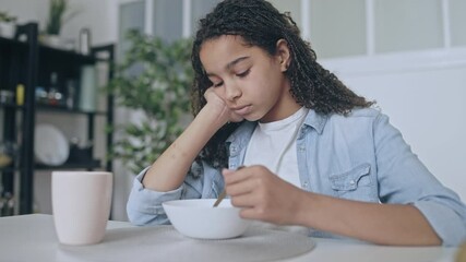 Upset afro-american teenage girl eating cereal, lack of appetite, mood swings