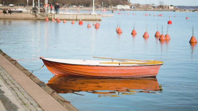 Small wooden rowboat with oars floating on the water while anchored in the dock