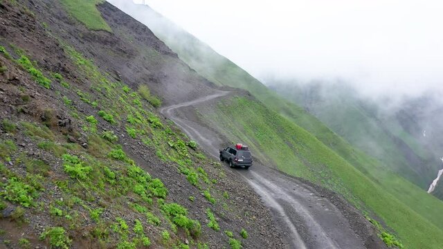 Vehicle driving on the edge of the mountains on one of the world's most dangerous roads, the of the Abano Pass in Tusheti Georgia. Wide cinematic drone shot.