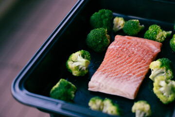 Fresh organic atlantic salmon fillet on baking tray with green broccoli florets as healthy food nutrition and keto diet