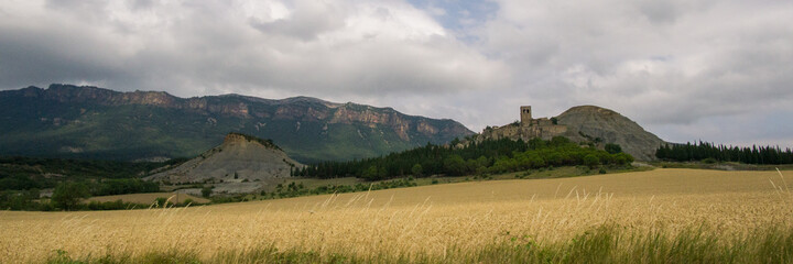 Old castle on a hill in countryside with wheat fields in foreground and mountains in background, Spain