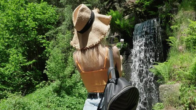 Young Travel Blogger Recording Video of Waterfall With Smartphone and Gimbal on Hot Summer Day in Countryside Landscape