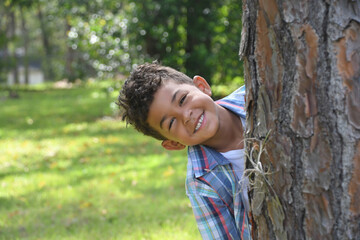 Smiling boy looking out from behind a tree.