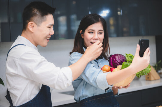husband and wife are smile together with mobile phone, mature indoor photo with girlfriend and guy standing in kitchen at apartment, friendship hugging for media retirement